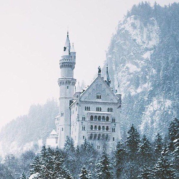 an old castle in the middle of a snowy forest with trees and snow covered mountains behind it