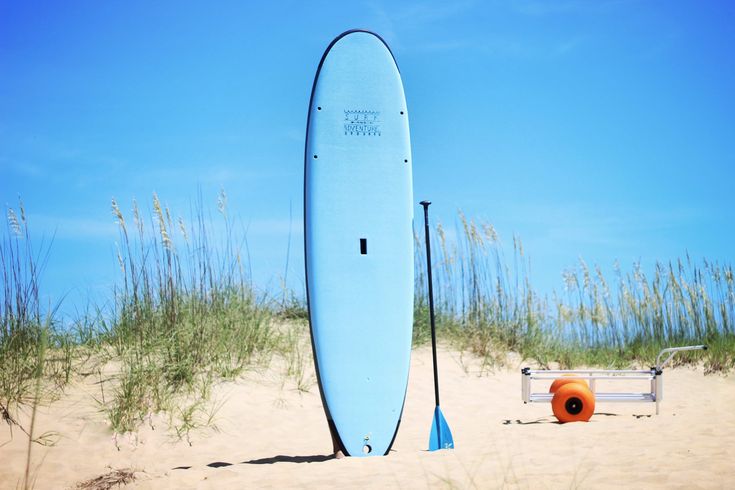 a blue surfboard sitting on top of a sandy beach next to tall grass and sea oats