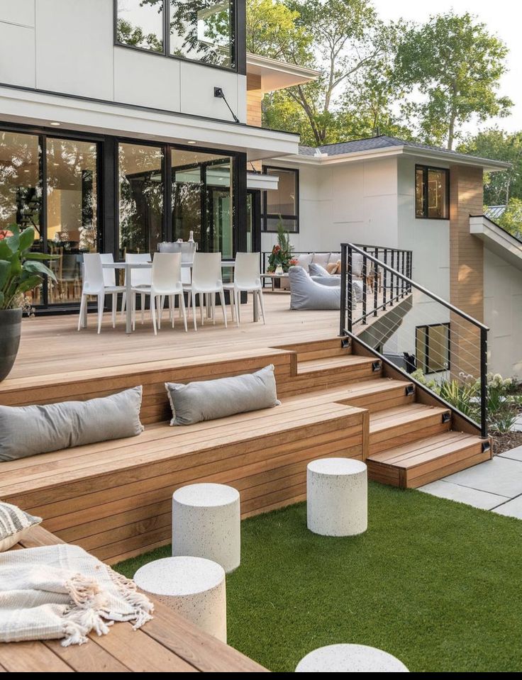 a wooden deck with white chairs and tables next to a large glass doored house