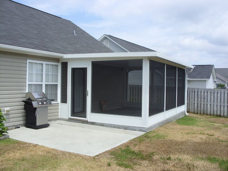 a small gray house with a screened porch and grill in the front yard, on a sunny day