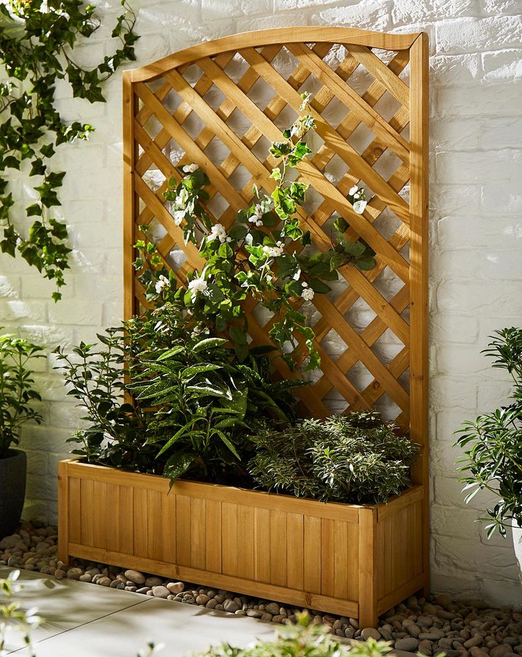 a wooden planter filled with plants next to a white brick wall and potted plants