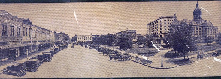 an old photo of a city street with cars parked on the side and buildings in the background