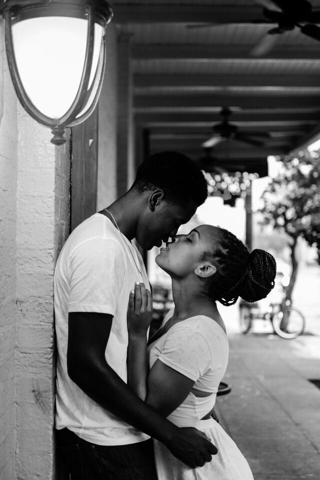 a man kissing a woman on the cheek while standing next to a wall with a lamp