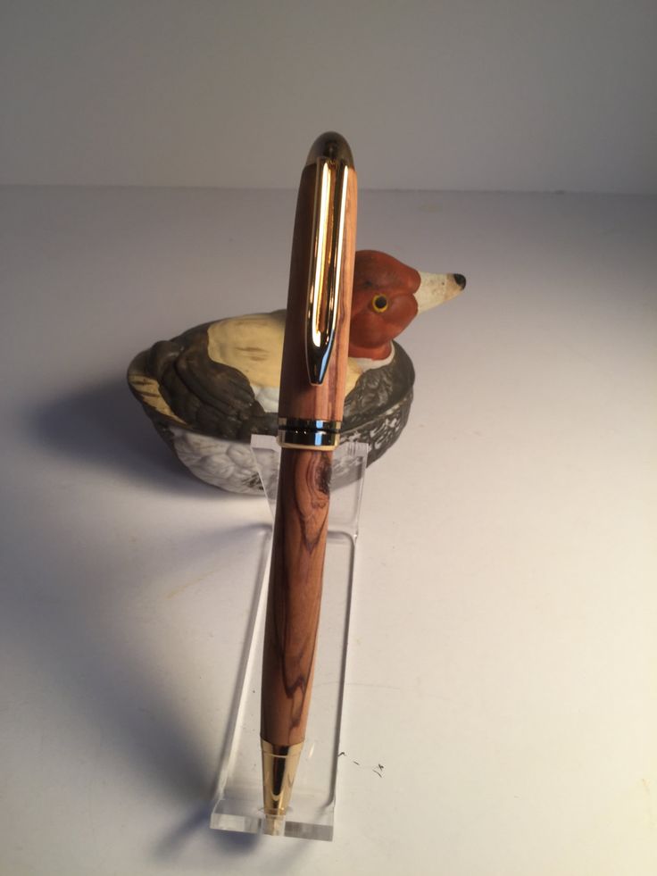 a fountain pen sitting on top of a wooden duck in a glass holder with a metal handle