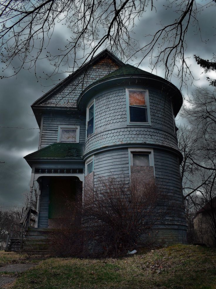 an old victorian house with dark clouds in the back ground and bare trees on either side