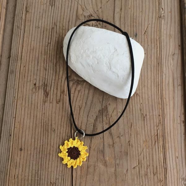 a yellow and brown sunflower on a black cord necklace next to a white rock