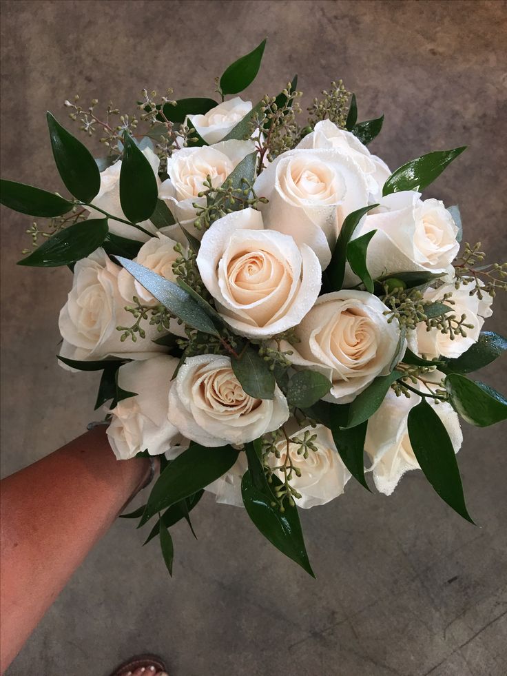 a bouquet of white roses and greenery in someone's hand on the ground