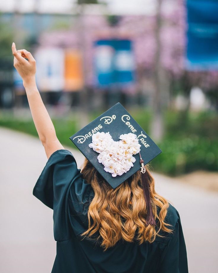 a woman wearing a graduation cap and gown raising her hand in the air with flowers on it