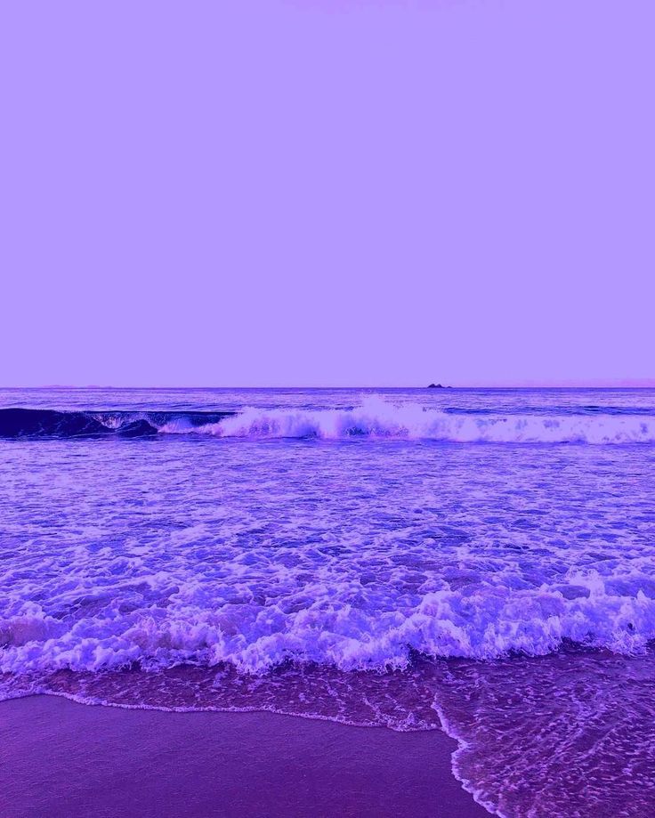 an ocean view with waves crashing on the shore and purple sky in the back ground