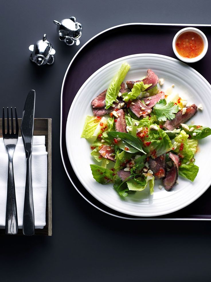 a white plate topped with meat and lettuce next to silverware on a table