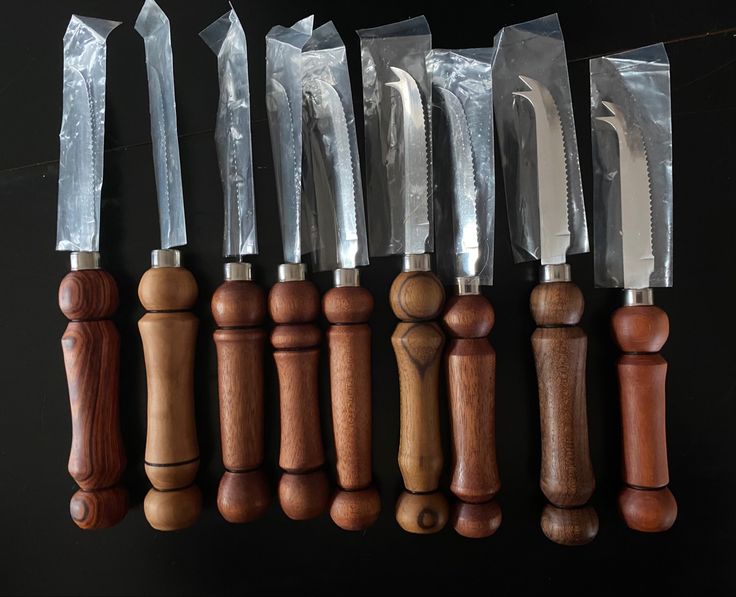 six knives are lined up in a row with plastic wrap on them, along with wooden handles