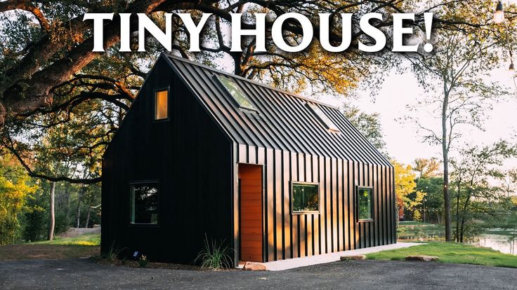 the tiny house is on display in front of a large tree and grassy area with trees