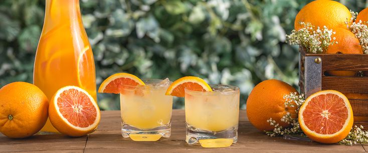 an orange drink with two glasses next to it and some sliced oranges on the table