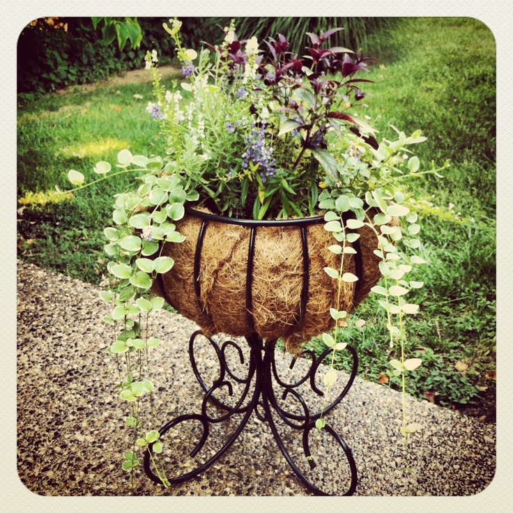 a planter filled with lots of flowers on top of a metal stand