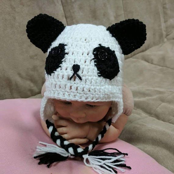 a baby wearing a panda bear hat on top of a pink blanket with black and white tassels