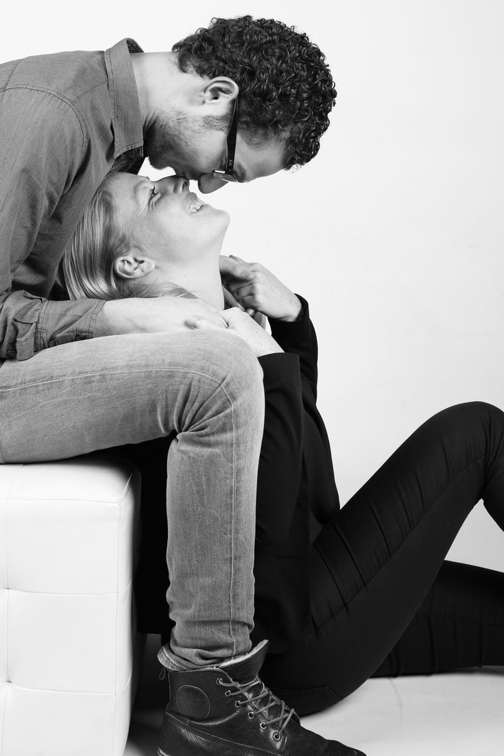 a man kissing a woman while sitting on top of a white couch in front of a wall