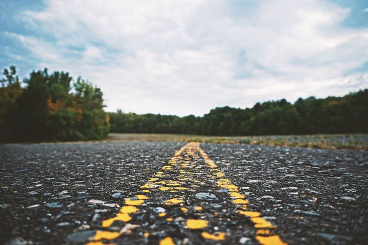 an empty road with yellow lines on it and trees in the backgrouds