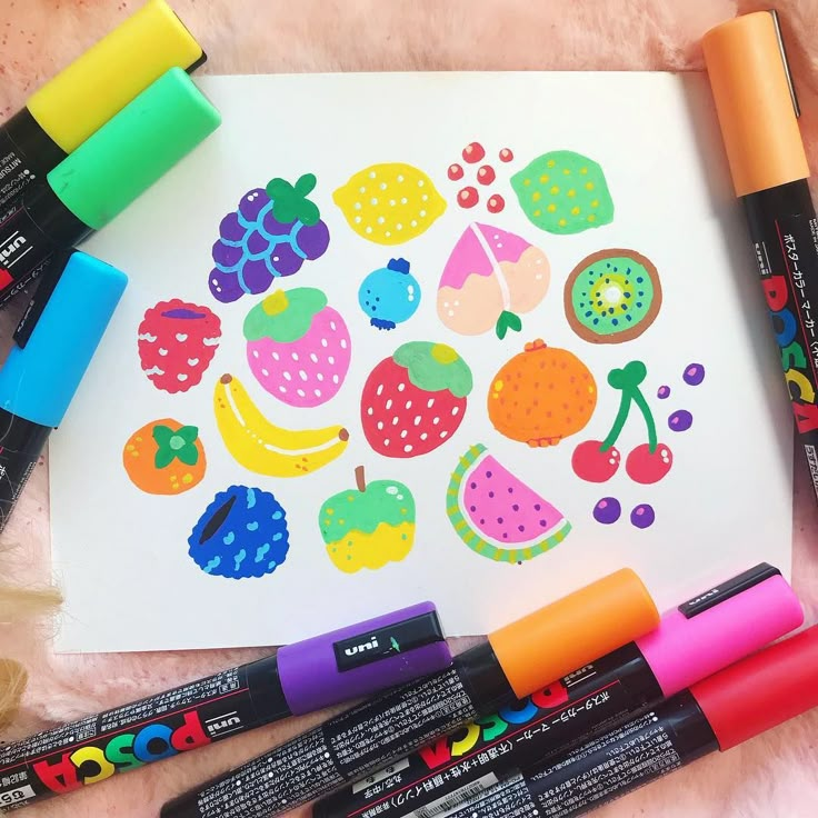 some markers are laying on top of a paper with fruit and berries drawn on it