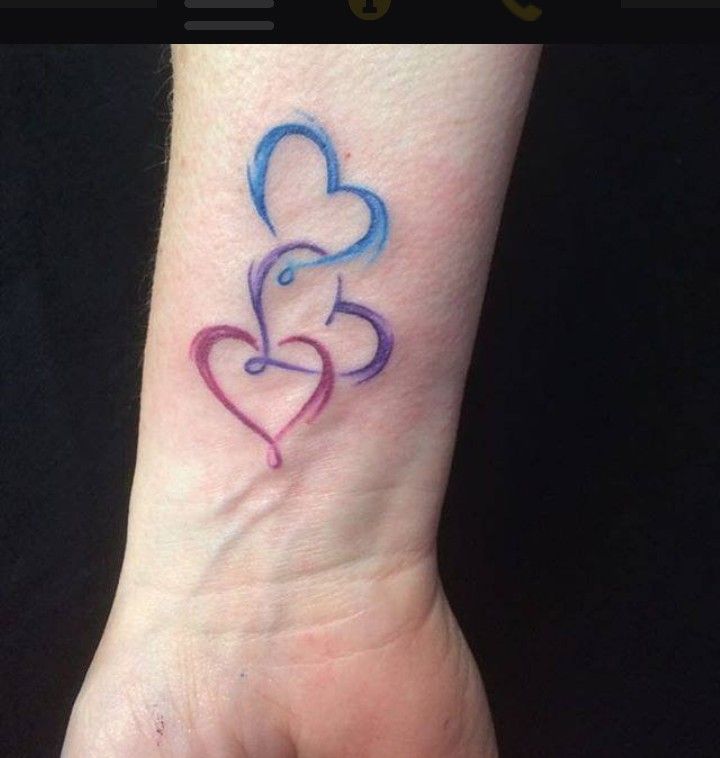 a small tattoo on the wrist of a woman with two hearts in blue and pink