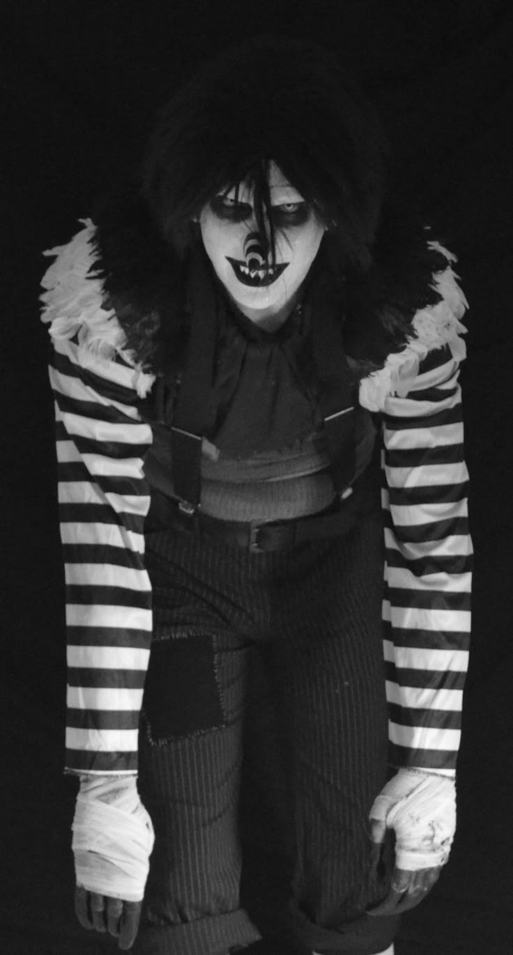 a man dressed up in clown makeup and striped clothes with his hands on his hips