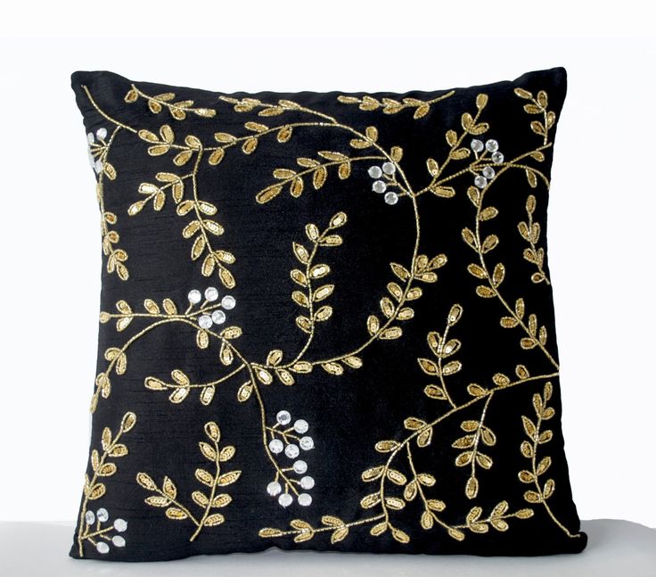 a black pillow with gold and white embroidered flowers on the front is sitting on a table