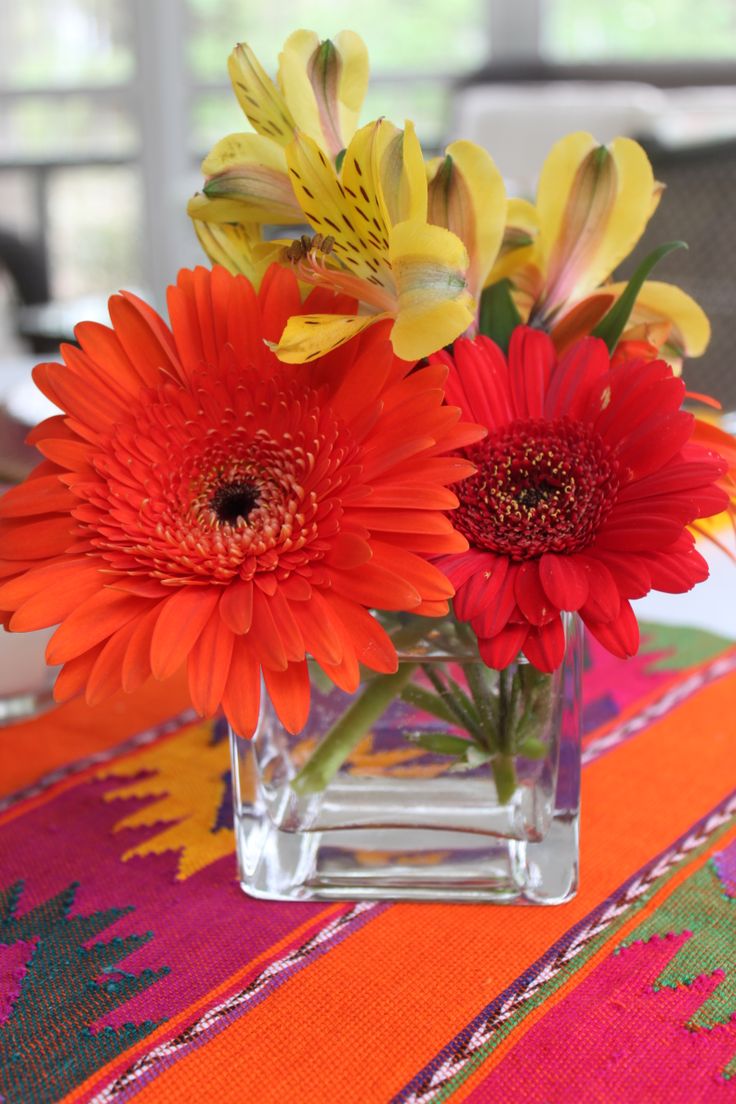 a vase filled with flowers sitting on top of a colorful table cloth next to a window