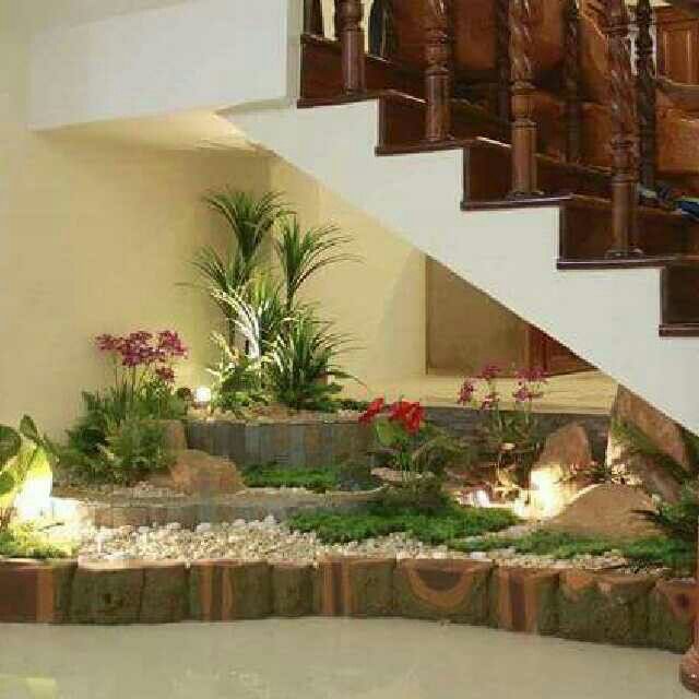 an indoor garden with plants and rocks under the stairs is lit up by lights on either side of the staircase