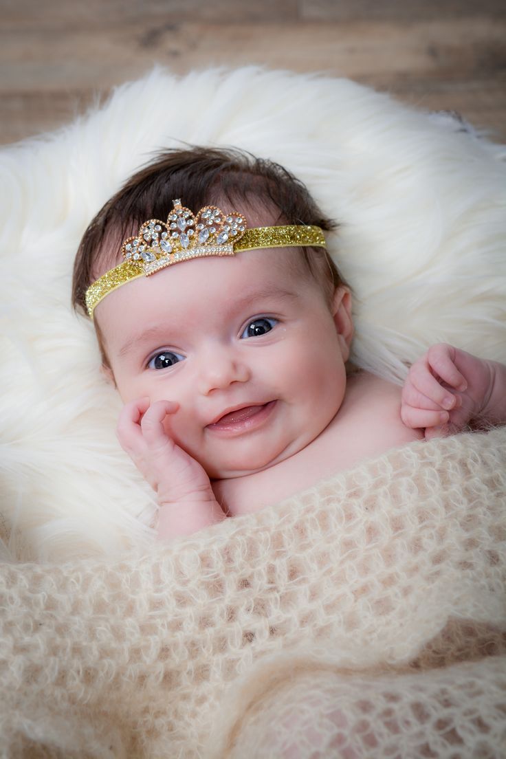 a baby wearing a tiara laying on top of a white fur covered blanket with her hands under her chin