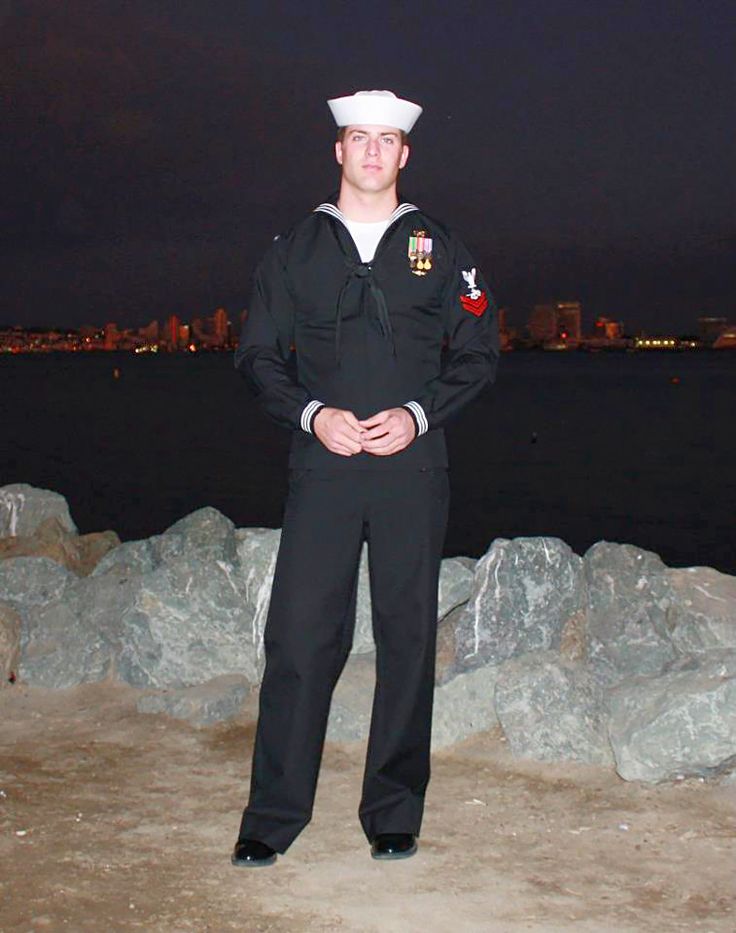 a man in a sailor's uniform is standing by some rocks and looking at the camera