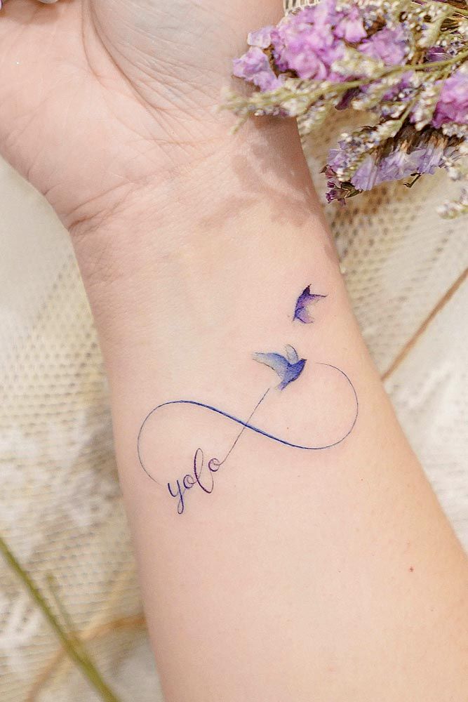 a woman's wrist with a tattoo on it and purple flowers in the background