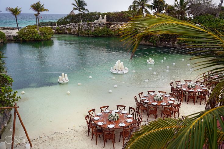 tables and chairs are set up on the beach for an outdoor dinner or party with sailboats in the water