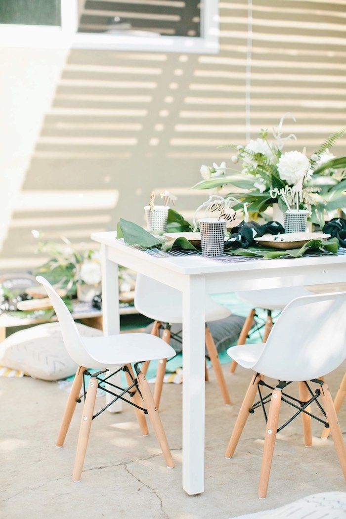 the table is set with white chairs and greenery