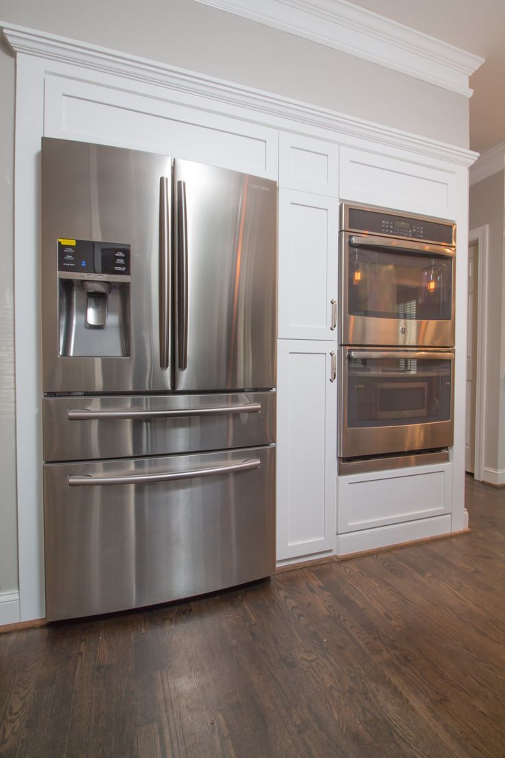 a stainless steel refrigerator and oven in a kitchen with white cabinets, hardwood floors, and wood flooring