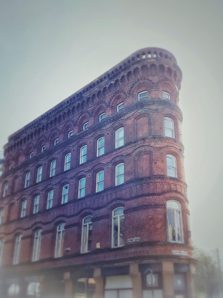 an old brick building with lots of windows on the top and bottom floor, in front of a cloudy sky