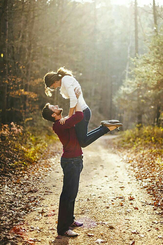 a man holding a woman on his back in the middle of a dirt road surrounded by trees