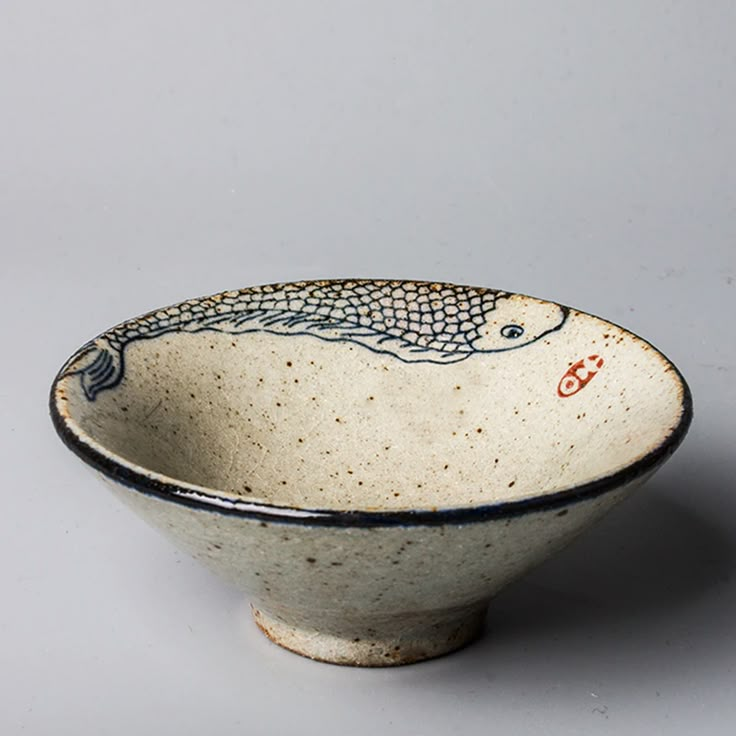 a white and black bowl with a fish design on the side, sitting on a gray surface