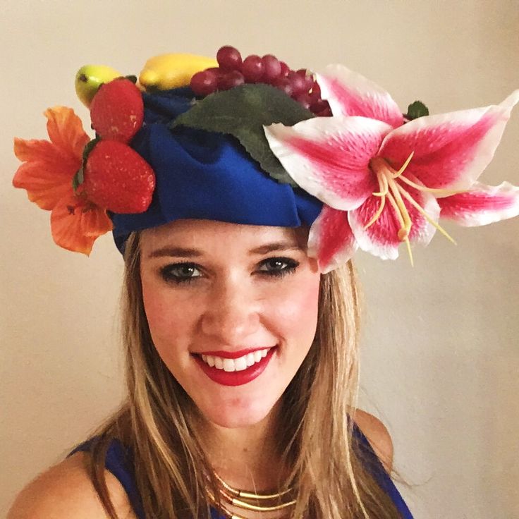 a woman wearing a blue hat with flowers and fruit on it's head is smiling at the camera