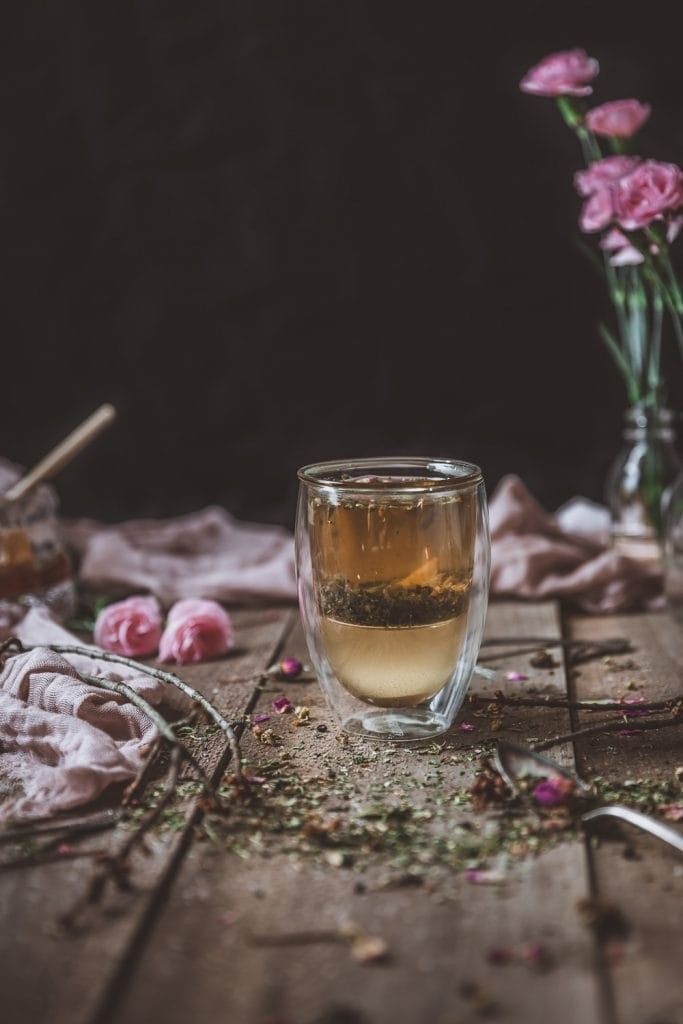 a glass filled with tea sitting on top of a wooden table next to pink flowers