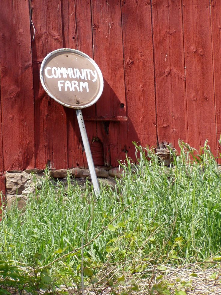 a sign that says community farm in front of a red wooden fence and green grass