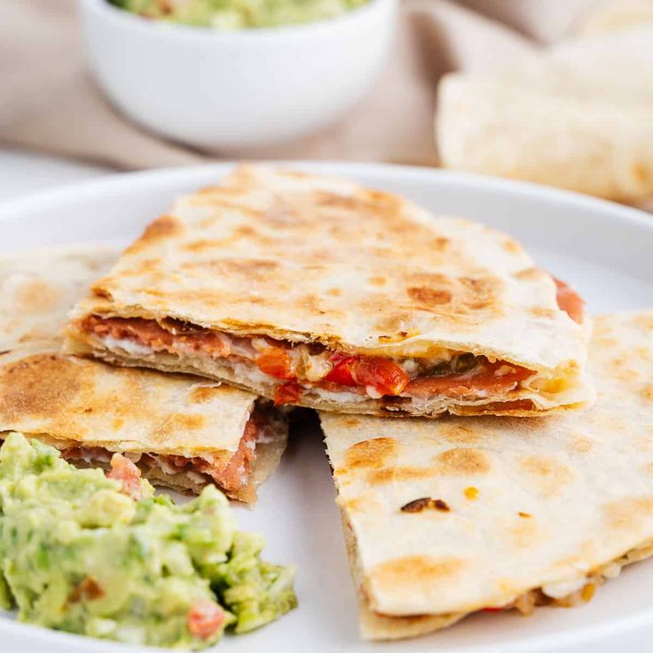 three quesadillas on a white plate with guacamole in the background