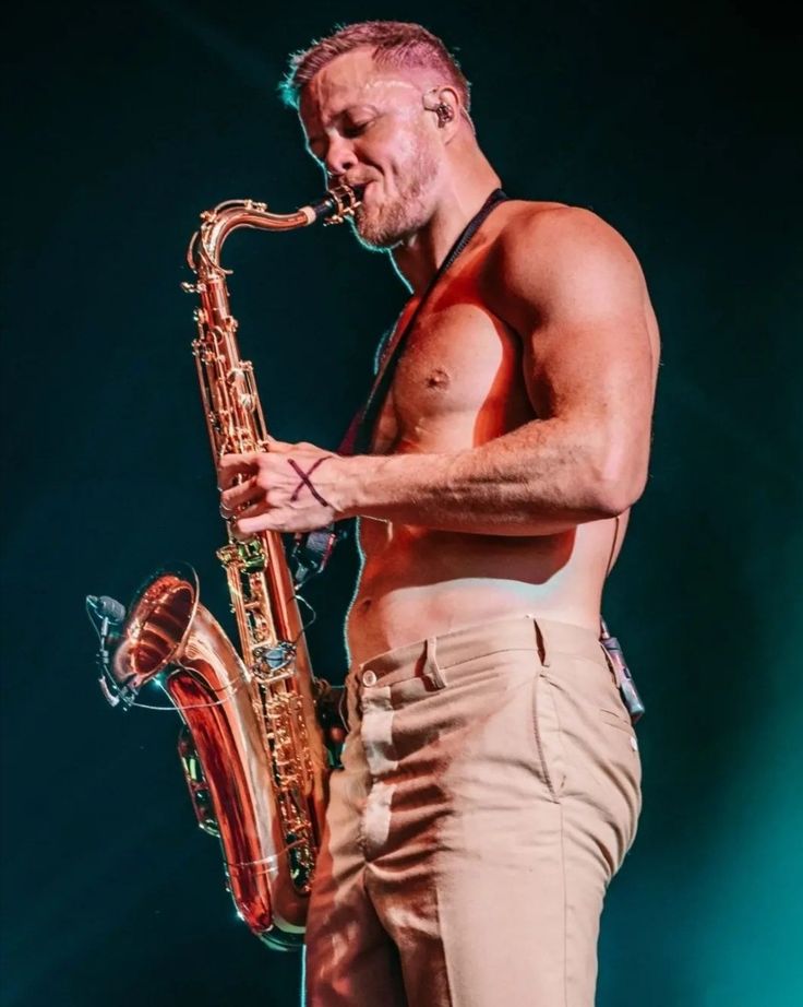 a shirtless man holding a saxophone in his right hand and wearing khaki pants