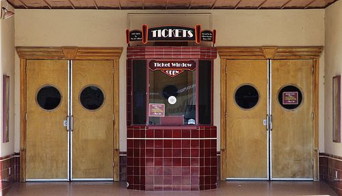 an empty building with three doors and two windows on each side, in front of the door is a ticket machine