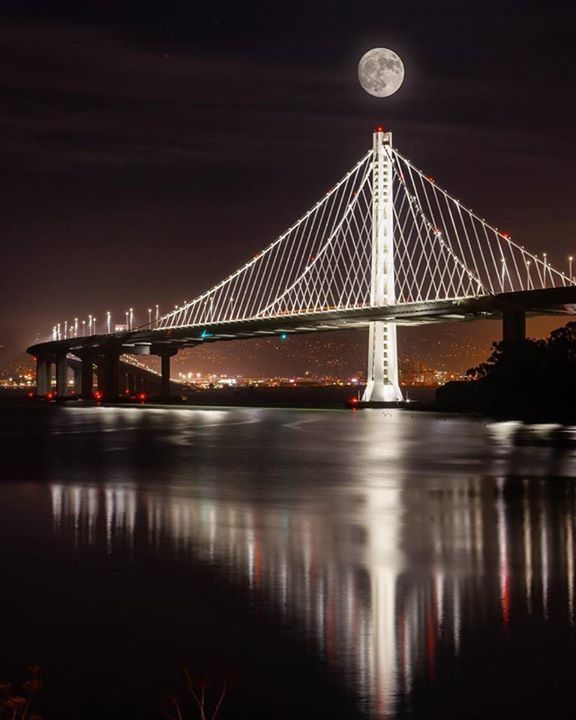 the moon is setting over the bay bridge