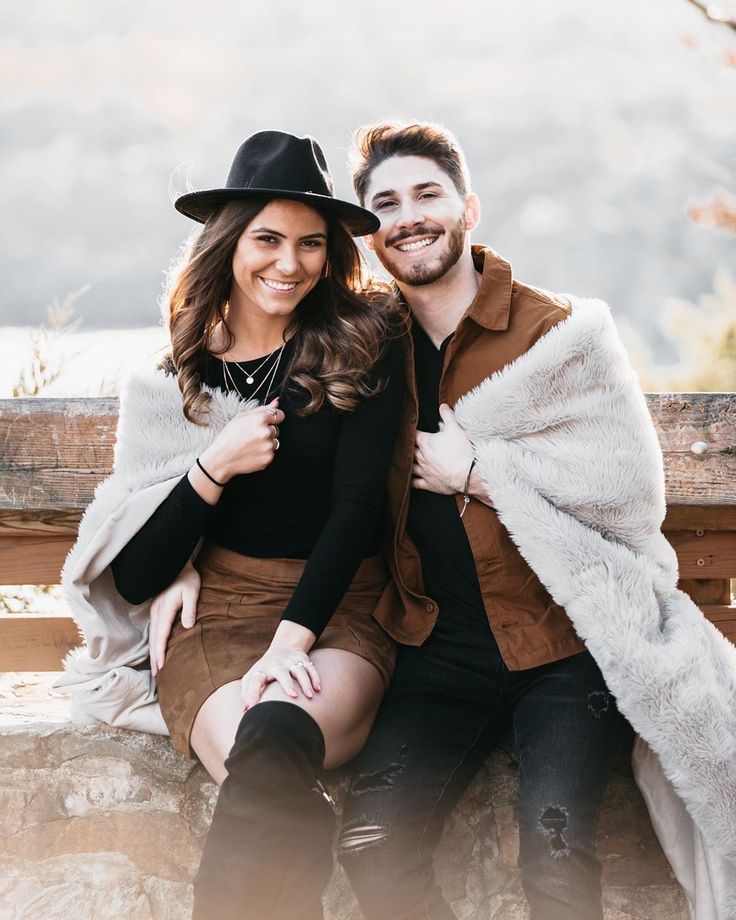 a man and woman sitting next to each other on a wooden bench with a fur coat over their shoulders