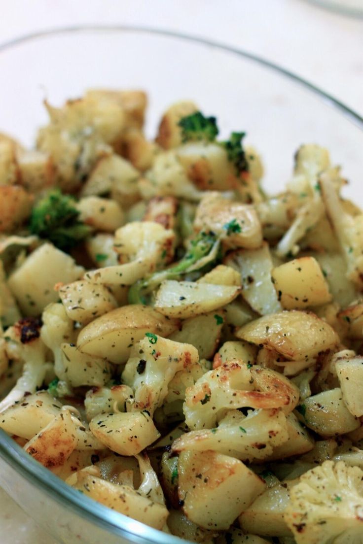 a glass bowl filled with potatoes and broccoli on top of a white table