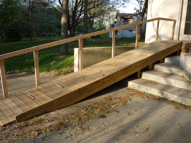 a wooden bench sitting on the side of a building next to a cement walkway and trees