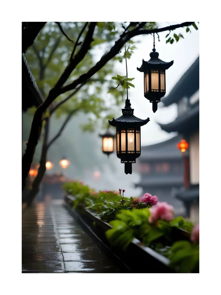 two lanterns hanging from the side of a tree in front of some flowers and trees