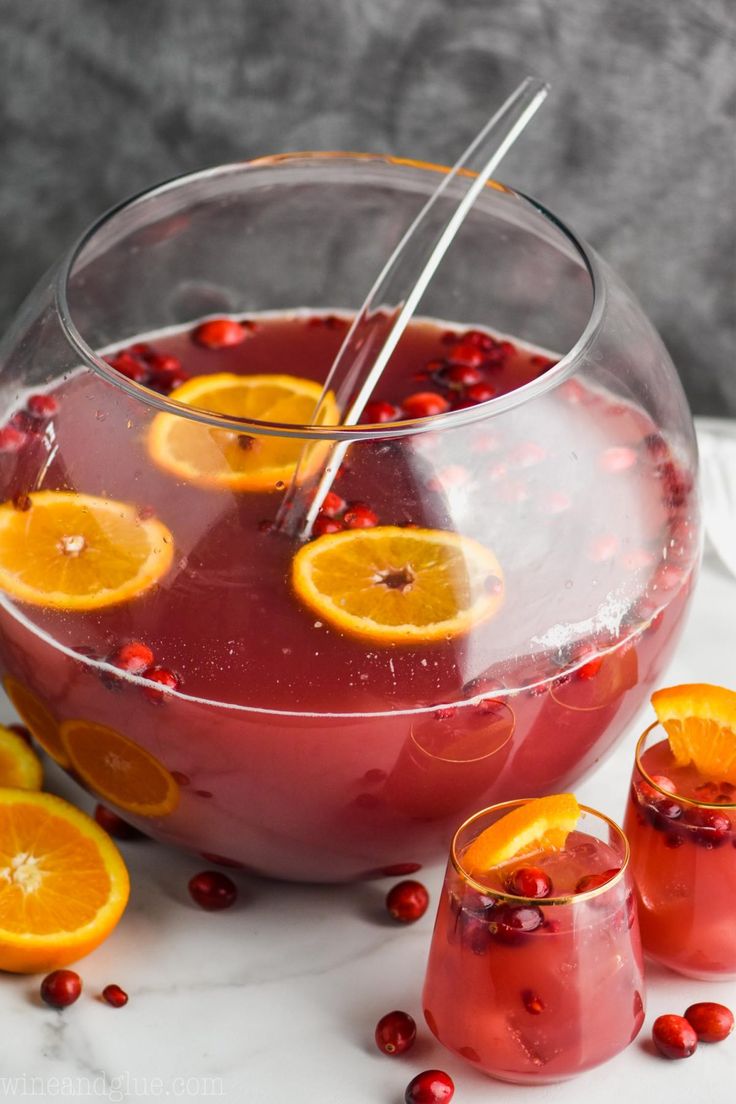 two glasses filled with red liquid and orange slices on the table next to some cranberries