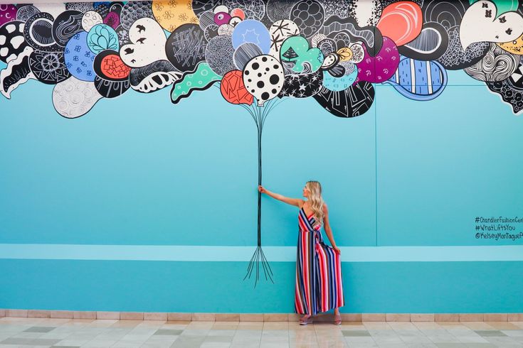 a woman is standing in front of a wall painted with cartoon heads and balloons on it