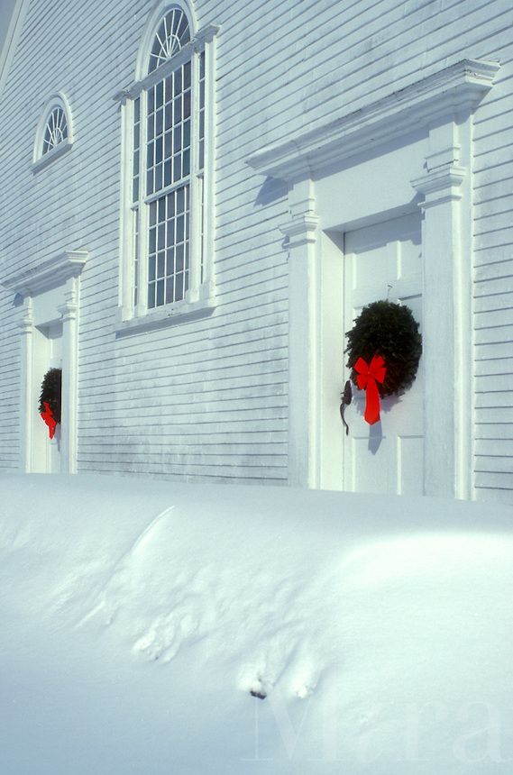 two wreaths are hanging on the front door of a white house with snow around them